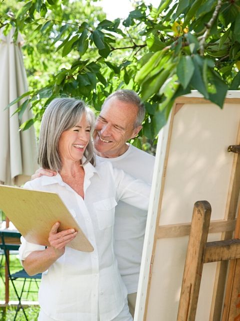 happy older married couple painting a canvas and laughing